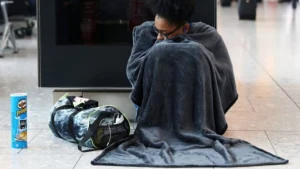 A person wrapped in a blanket beside their belongings, illustrating the consequences of disruption.